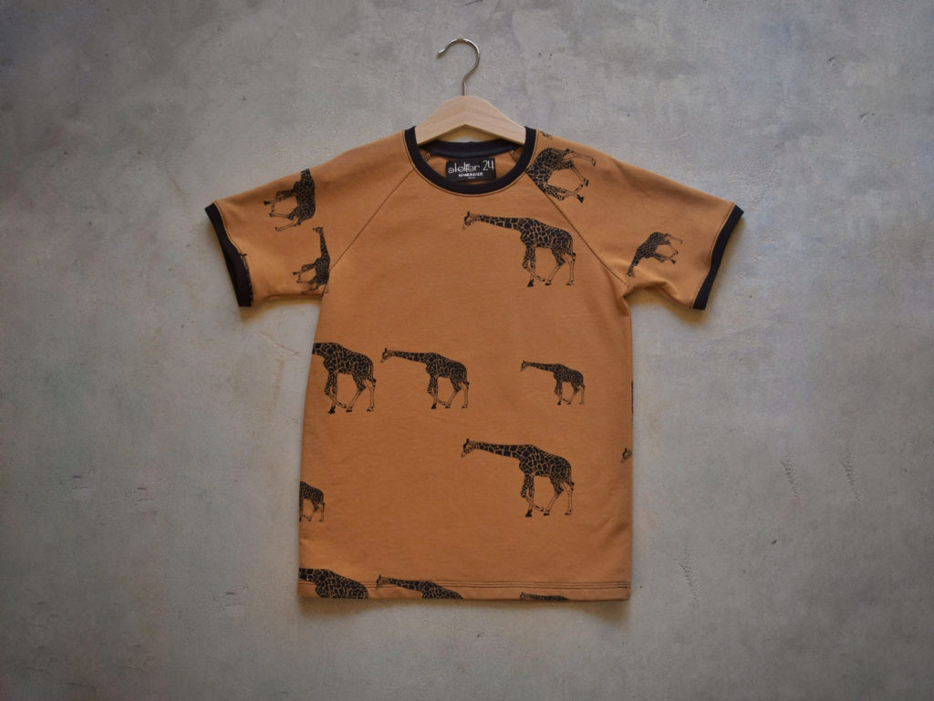 T-shirt pour garçons à fond ocre et motif girafes. Bord-côte noir à l'encolure et aux manches.
