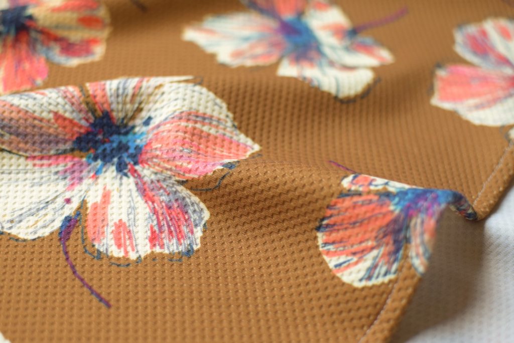 Détail de la texture de la robe évasée en jersey gaufré à grandes fleurs, fond couleur camel.