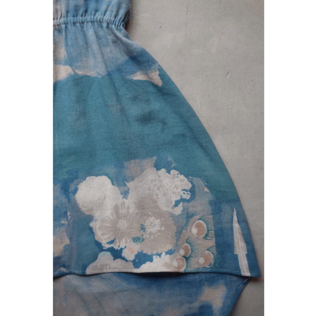 Détail d'une robe asymétrique cintrée bleue, à motif partiellement floral, sans manche.