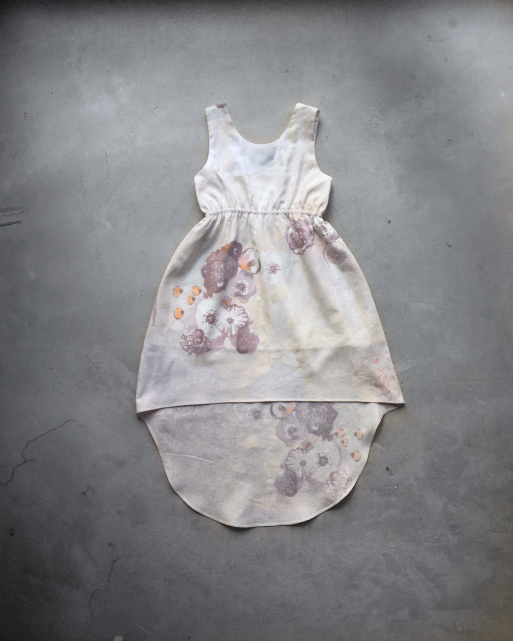 Robe asymétrique cintrée sans manche pour petite fille. Dans les tons écru avec un motif floral.